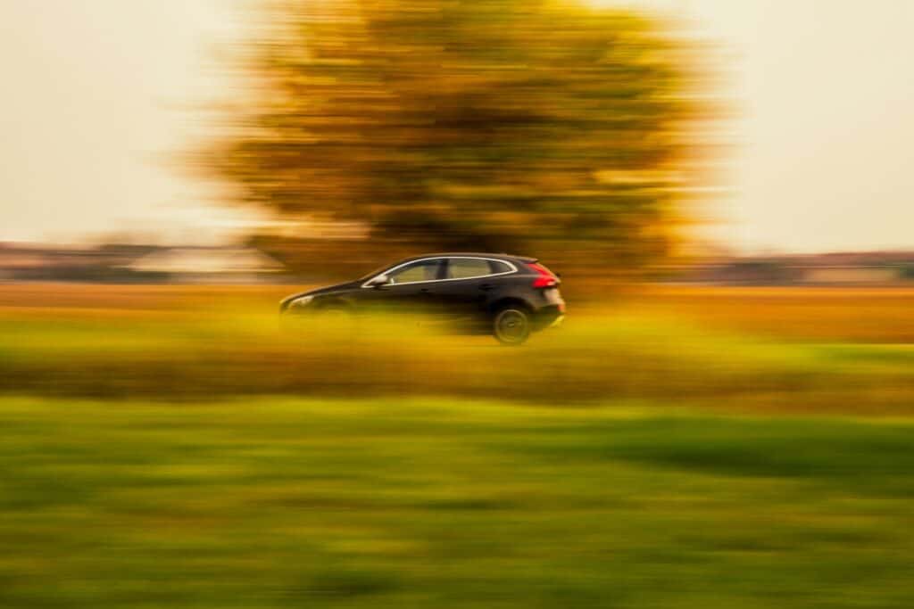 A black car moves quickly through a blurred landscape with green grass and a yellowish-orange background.